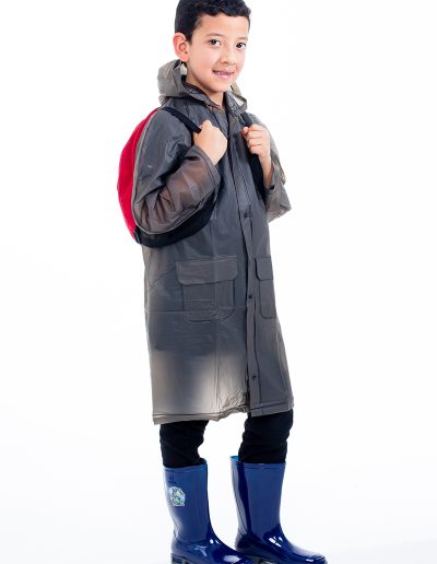 Kid wearing a transparent black waterproof coat, red suitcase, and blue boots