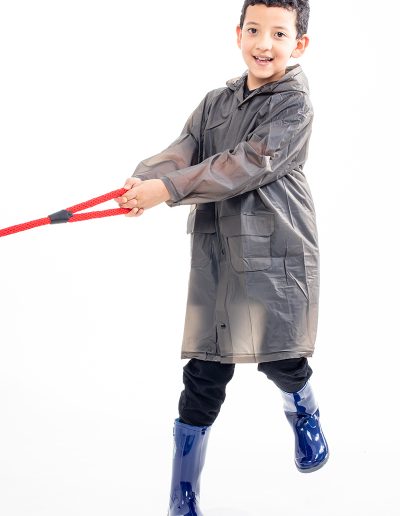 Kid wearing a transparent black waterproof coat and blue boots, pulling a red rope