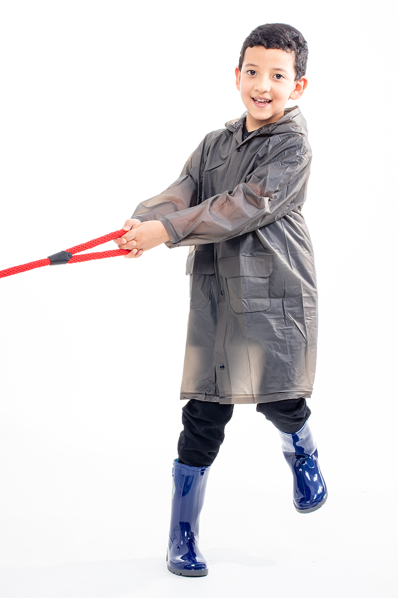 Kid wearing a transparent black waterproof coat and blue boots, pulling a red rope